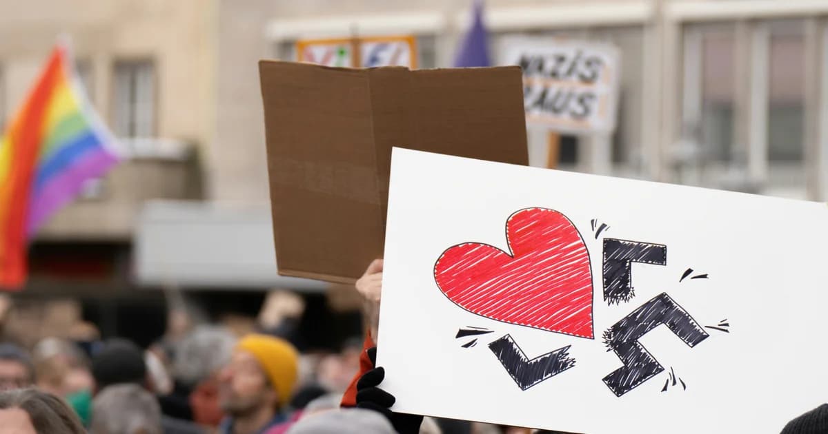 Un zoom sur une pancarte lors d'une manifestation qui réprésente un symbole na*i cassé par un coeur